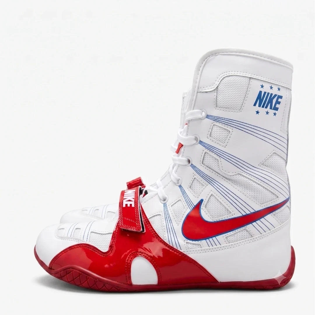 A Nike high-top boxing shoe in white, red, and blue, featuring a red Swoosh, a red strap with a white Nike logo, and blue Nike branding on the ankle collar.