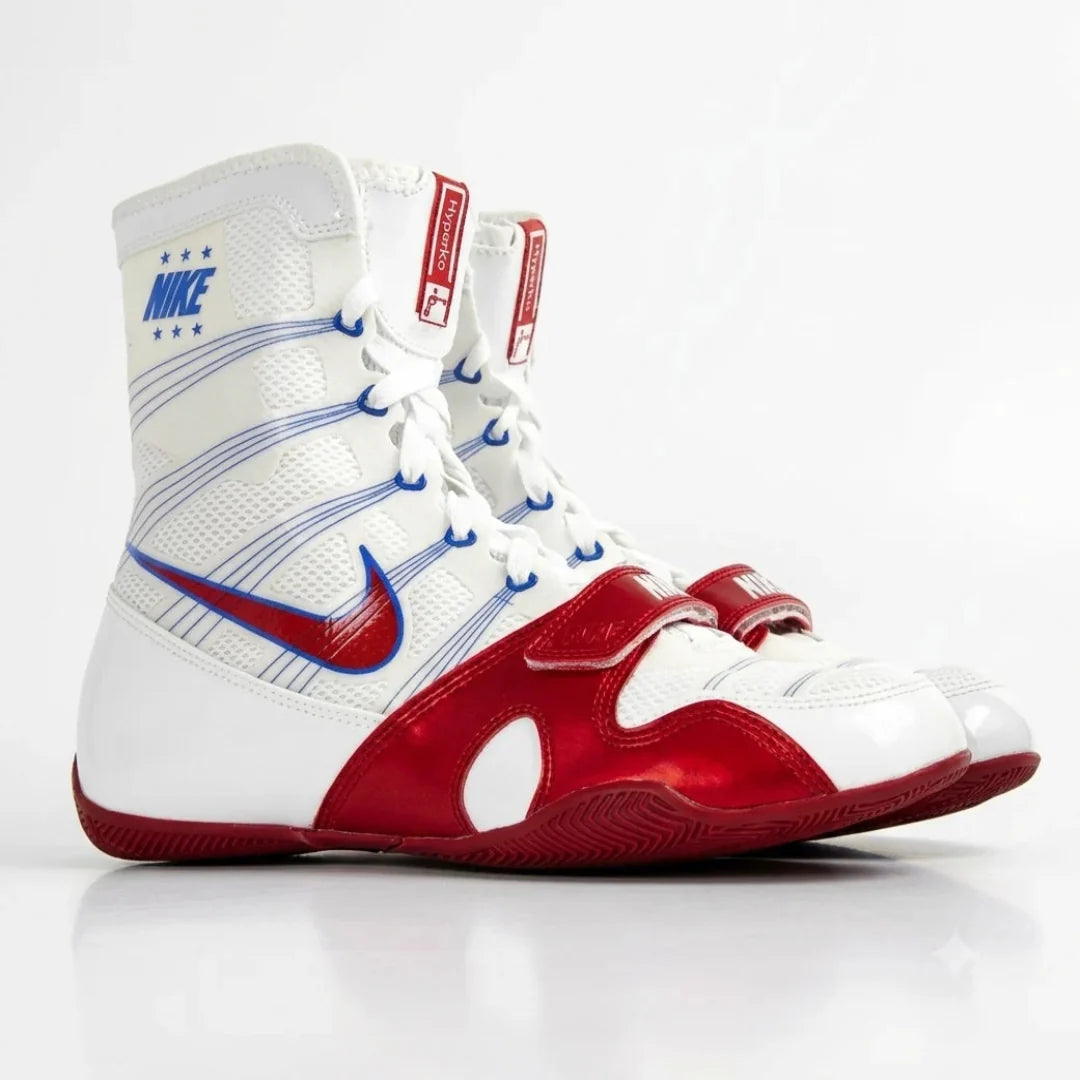 A pair of Nike high-top boxing shoes in white, red, and blue, featuring a white mesh upper with blue stripe details, a red Swoosh, and red toe caps, shown on a white background.